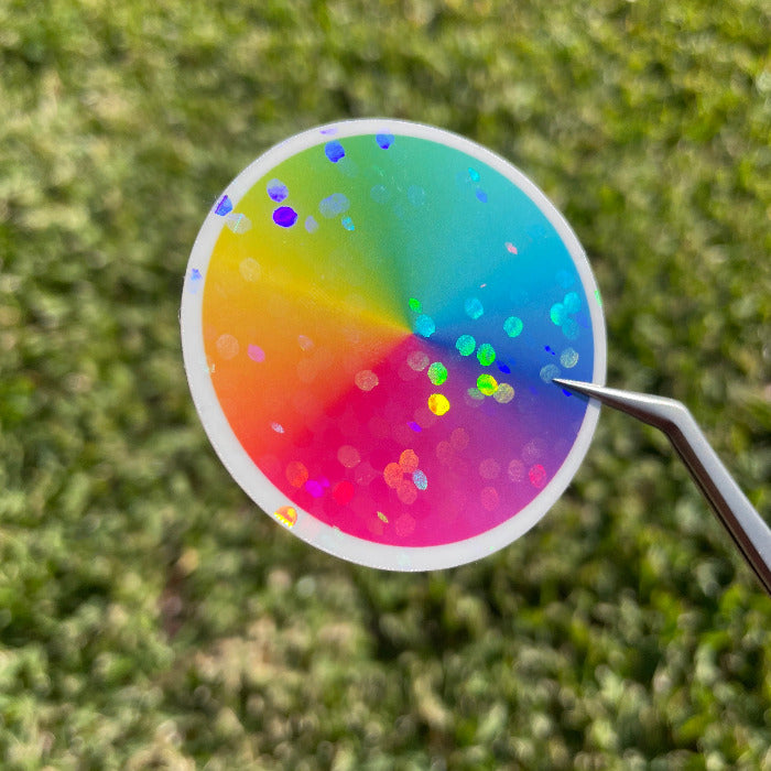 Top view of a colour wheel sticker in natural sunlight, showing the design of the disco dots holographic cold laminate dancing in the sunlight. The design features large rainbow speckles.