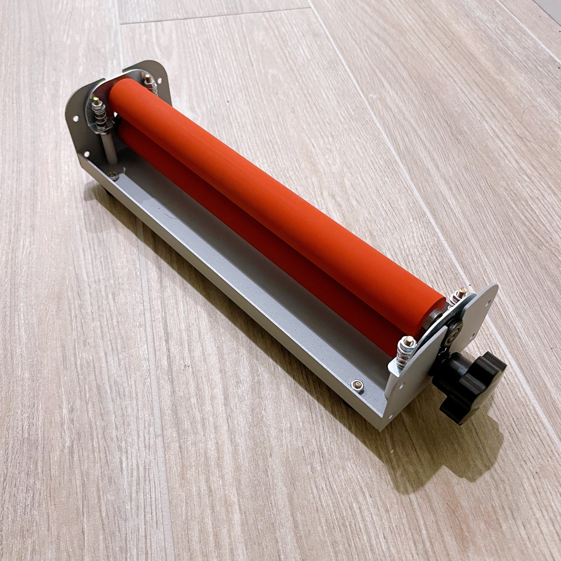 Angled top view of a compact cold laminator machine for A4 paper with orange rollers. This machine is used for applying cold laminate sheets to sticker paper.
