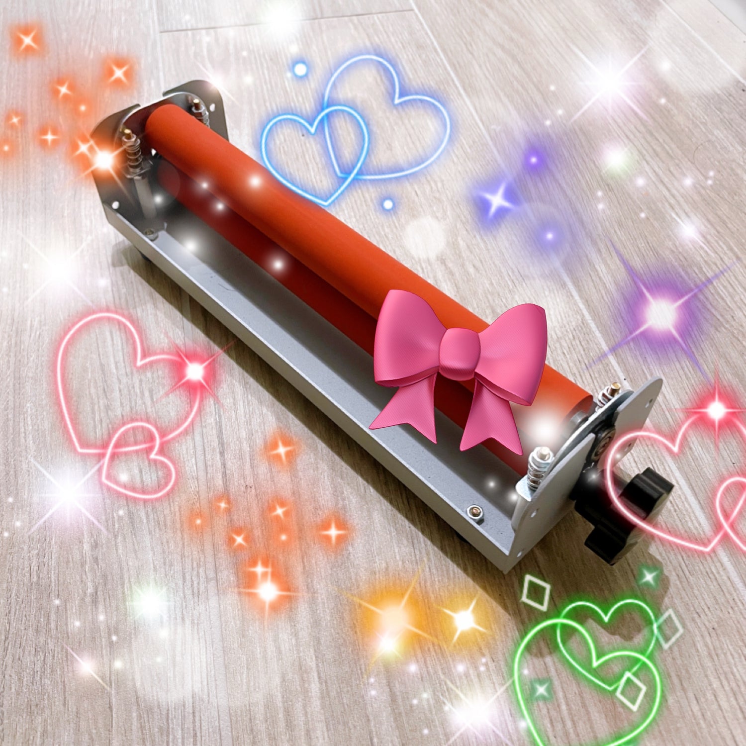Angled top view of a compact cold laminator machine for A4 paper with orange rollers, decorated with pictures of hearts and bows. This machine is used for applying cold laminate sheets to sticker paper.