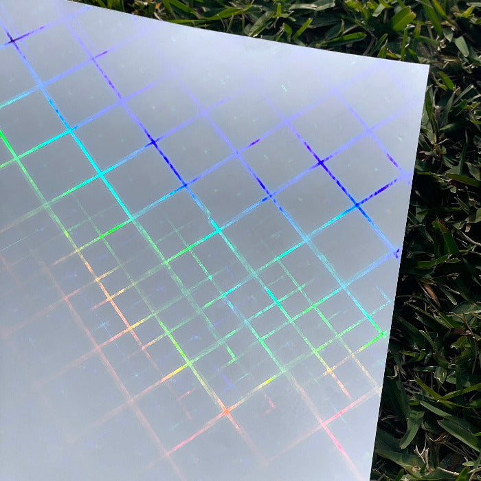 Top view of a piece of the cross beams holographic cold laminate sheet offered by Stickybeaky. The sunlight is hitting the sheet and showing the holographic criss-crossing pattern with some thicker lines and some thinner lines.