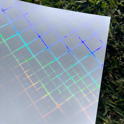 Top view of a piece of the cross beams holographic cold laminate sheet offered by Stickybeaky. The sunlight is hitting the sheet and showing the holographic criss-crossing pattern with some thicker lines and some thinner lines.